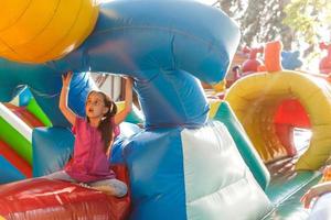 menina feliz se divertindo muito em um castelo de salto durante o deslizamento. foto