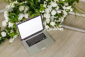 mesa de escritório em casa com laptop de tela em branco, lindas rosas e buquê de eucalipto, blog, site ou conceito de mídia social foto