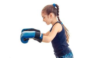 menina com rabo de cavalo fica de lado e estendeu a mão em grandes luvas de boxe foto