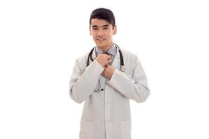 bonito moreno médico de uniforme com estetoscópio no pescoço posando na câmera isolada no fundo branco foto