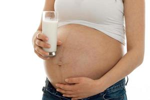 mulher grávida posando com copo de leite isolado no fundo branco foto