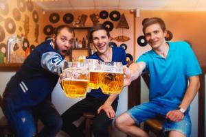 três homens alegres brindam com copos de cerveja em um bar foto