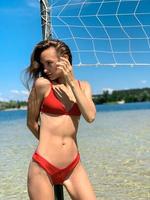 mulher jovem e bonita em maiô vermelho posando perto da rede de vôlei de praia foto