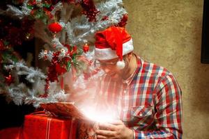 milagre de natal. nerd abre seu presente com chapéu de Papai Noel foto