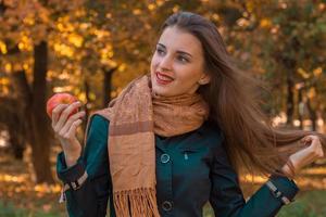linda garota com cabelo comprido e um cachecol marrom mantém a maçã na mão desvia o olhar sorrisos foto