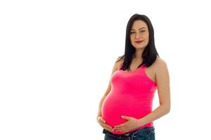 linda jovem grávida em uma camiseta rosa mantém a barriga das mãos foto