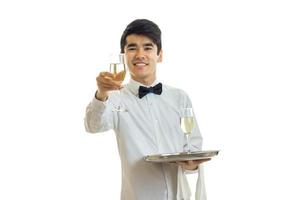 jovem garçom bonito em uma camisa branca se estende para a frente copo de vinho e sorrindo foto