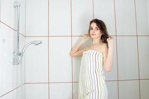 menina de pé em uma banheira em uma toalha grande e alisa o cabelo foto