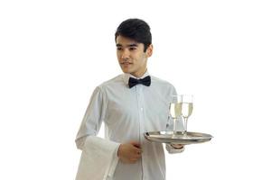 jovem garçom bonito em uma camisa branca, segurando uma bandeja com taças de champanhe foto