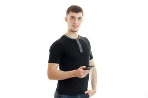 cara bonito alegre em uma camiseta preta segurando um telefone e olhando diretamente foto