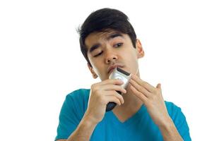 cara jovem engraçado com cabelo preto olha para a distância e raspa cuidadosamente o aparador de bigode é isolado em um fundo branco foto