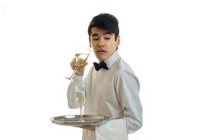 lindo garçom engraçado fica de lado em uma camisa branca olha para a boca aberta e segurando um copo de vinho foto