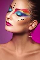 retrato vertical de uma linda garota adulta com maquiagem multicolorida em fundo roxo foto