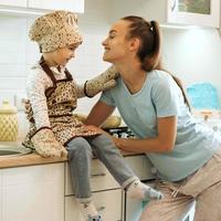 menina bonitinha caseira com sua linda mãe faz panquecas na cozinha branca. foto