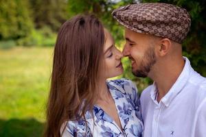 retrato de um jovem casal apaixonado tocando seus narizes e sorrisos no parque verde foto