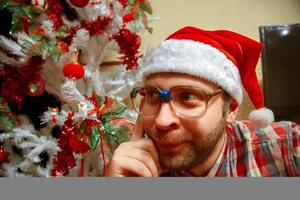 retrato engraçado de hipster em copos e chapéu de Papai Noel perto de árvore de natal foto