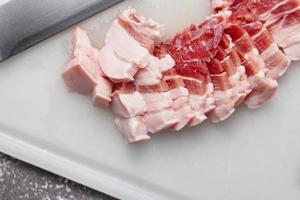 carne de porco entremeada é cortada em uma tábua de cortar branca na cozinha foto