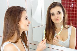 jovem mulher bonita escovando os dentes na frente do espelho foto