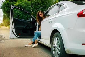 senhora glamourosa com óculos senta-se em um carro branco grande e bonito foto