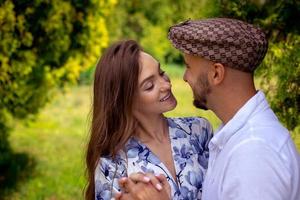 jovem lindo casal apaixonado sorri um para o outro no jardim verde foto