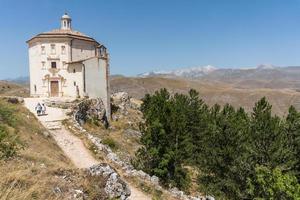 calascio, itália-9 de agosto de 2021-pessoas em frente à igreja de santa maria della pieta no caminho que leva a rocca calascio durante um dia ensolarado foto