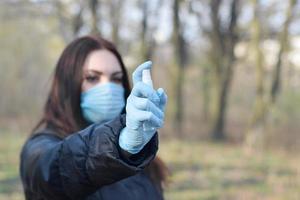 jovem com máscara protetora mostra frascos de spray desinfetante ao ar livre em madeira de primavera foto