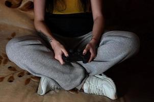 controlador de jogo preto moderno nas mãos de uma jovem sentada foto