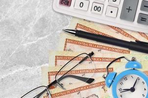 Notas de 100 pesos dominicanos e calculadora com óculos e caneta. empréstimo comercial ou conceito de temporada de pagamento de impostos. hora de pagar impostos foto