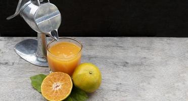 suco de laranja em vidro e frutas cítricas frescas ao redor com espremedor de frutas espremedor de mão na mesa de madeira foto