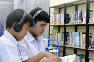 fucus suave de dois estudantes asiáticos estão ouvindo mídia, lendo e consultando sobre o livro favorito na biblioteca da escola foto