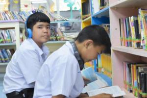 fucus suave de dois estudantes asiáticos estão ouvindo mídia, lendo e consultando sobre o livro favorito na biblioteca da escola foto