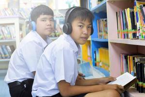 fucus suave de dois estudantes asiáticos estão ouvindo mídia, lendo e consultando sobre o livro favorito na biblioteca da escola foto