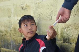 menino aprendendo a fumar sozinho na área atrás da cerca da escola, que é um lugar escondido para as pessoas, má influência da escola secundária ou da vida escolar, vício. foto