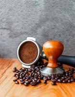 equipamento de porta-filtro de ferramenta de café barista com adulteração e grãos de café torrados escuros na mesa de madeira em uma cafeteria foto