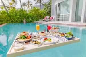 café da manhã na piscina, café da manhã flutuante no luxuoso resort tropical. mesa relaxante na água calma da piscina, café da manhã saudável e prato de frutas na piscina do resort. estilo de vida de luxo de praia tropical foto