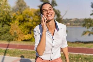 jovem mulher usando telefone celular no parque pelo rio foto