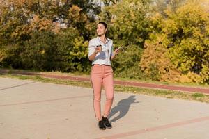 mulher jovem feliz com café ouvindo música no smartphone e andando no passeio foto