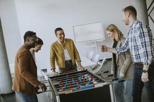 jovens empresários multiétnicos casuais jogando futebol de mesa e relaxando no escritório foto
