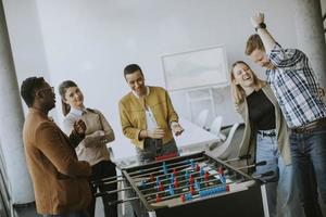 jovens empresários multiétnicos casuais jogando futebol de mesa e relaxando no escritório foto
