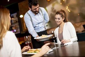 jovem garçom servindo comida para clientes do sexo feminino no restaurante foto