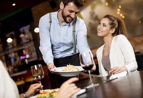 jovem garçom servindo comida para clientes do sexo feminino no restaurante foto