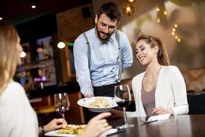 jovem garçom servindo comida para clientes do sexo feminino no restaurante foto