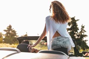 amigos se divertindo na viagem de carro ao redor do mundo. casal apaixonado com os braços para cima em um carro conversível. foto