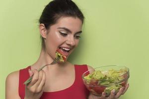 retrato de uma menina lúdica feliz comendo salada fresca de uma tigela foto