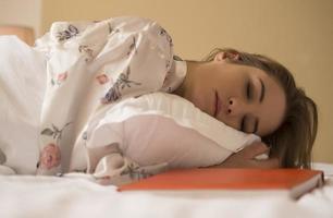 pacífica serena bela jovem vestindo pijama deitado dormindo relaxando dormindo na cama branca aconchegante no travesseiro macio descansando foto