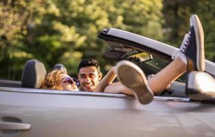 amigos se divertindo na viagem de carro ao redor do mundo. casal apaixonado com os braços para cima em um carro conversível. foto