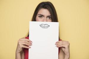 jovem mulher sorridente segurando uma folha de papel em branco para publicidade foto