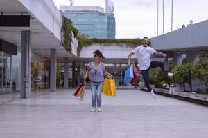 retrato de um jovem casal caucasiano alegre homem e mulher segurando muitos sacos de papel depois de fazer compras enquanto caminhava e conversava na rua. casal de família feliz com pacotes ao ar livre. conceito de compra foto