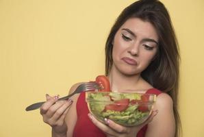 retrato de uma menina lúdica feliz comendo salada fresca de uma tigela foto