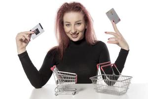 mulher feliz segurando cartões de crédito e um pequeno carrinho de compras vazio isolado no fundo branco foto
